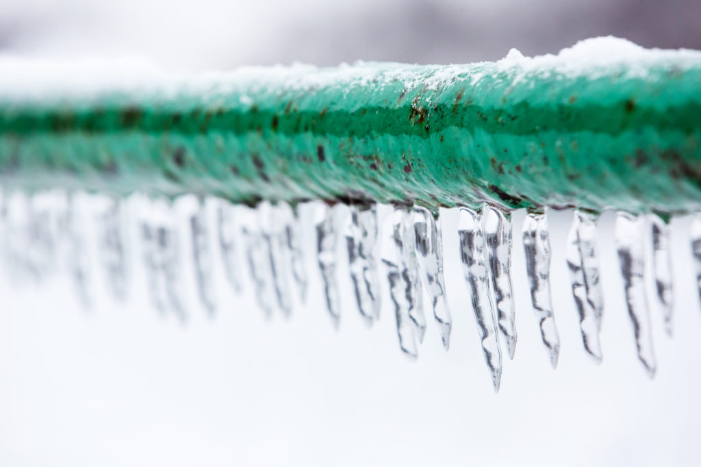 Focused view of a frozen pipe with icicles forming.